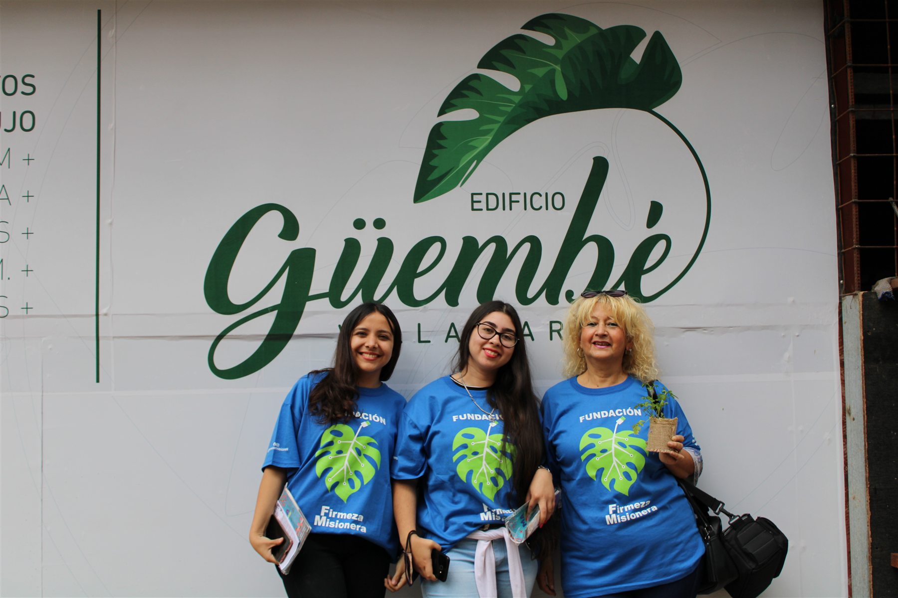 Tres voluntarias y promotoras con remeras de la Fundación frente a un cartel de Edificio Guembé